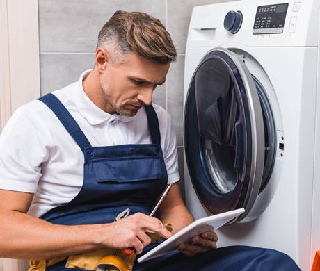 adult repairman holding screwdriver and using digital tablet while repairing washing machine in