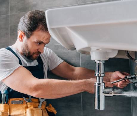 focused male plumber in working overall fixing sink in bathroom