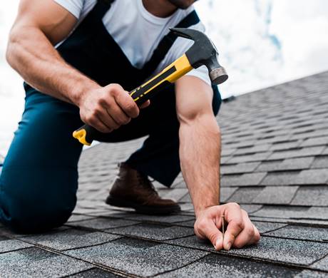 cropped view of handyman in uniform holding hammer while repairing roof